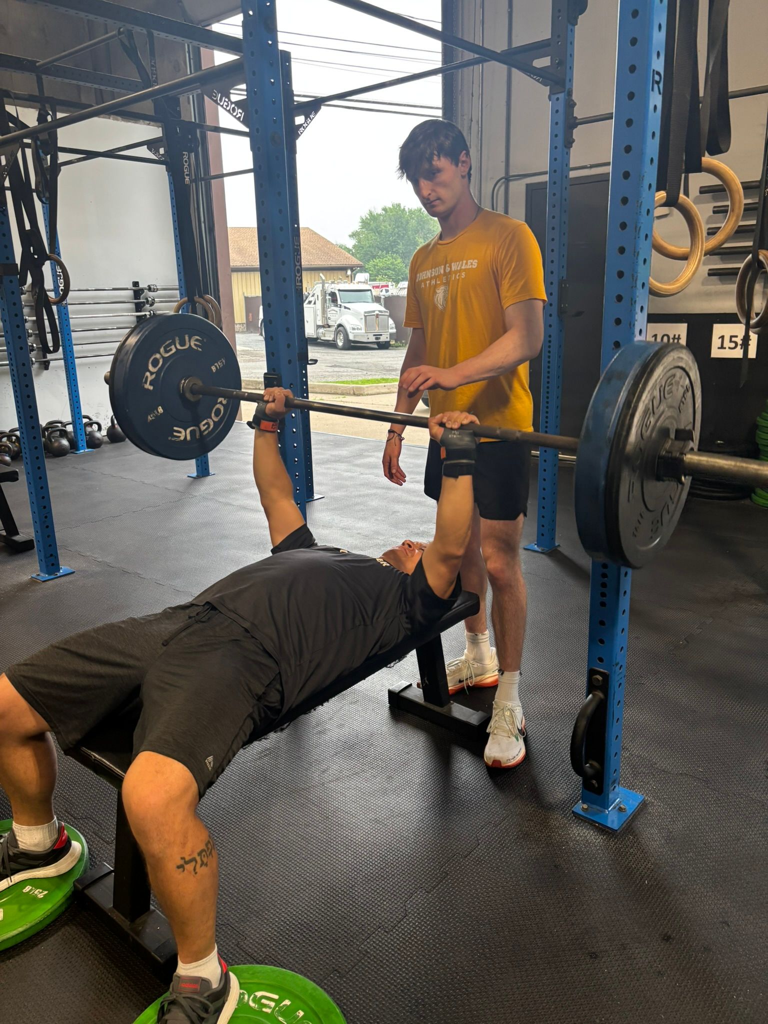 Man bench-pressing with spotter at a gym. Spotter watches intently.
