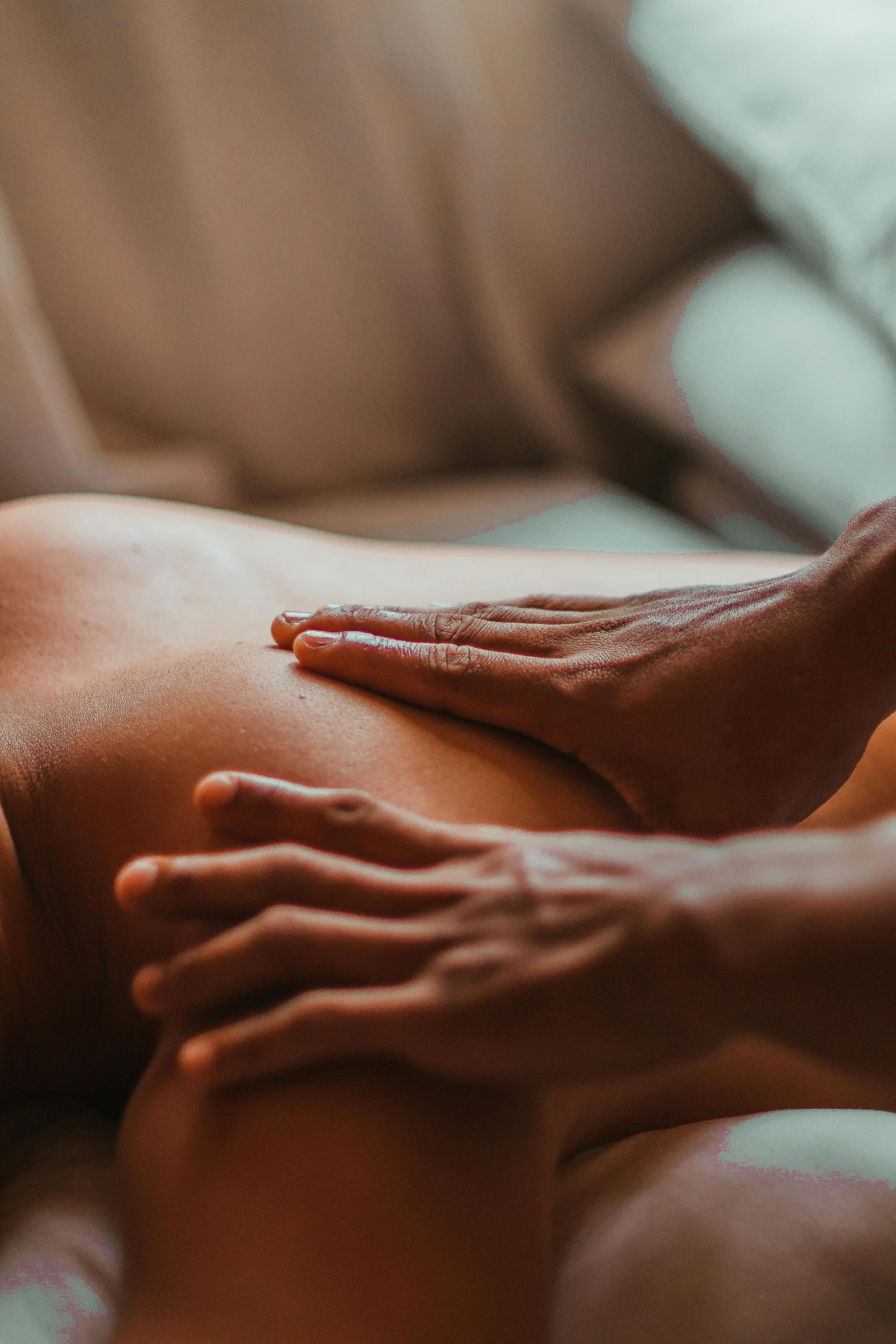 Hands giving a massage on a person's back, with oils applied, in a relaxed setting.
