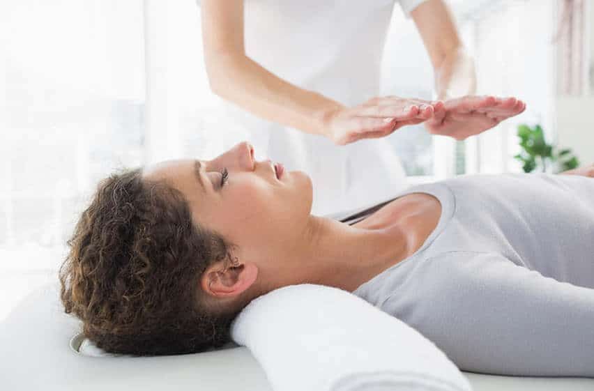 Woman receiving energy healing with hands hovering above her, indoors.