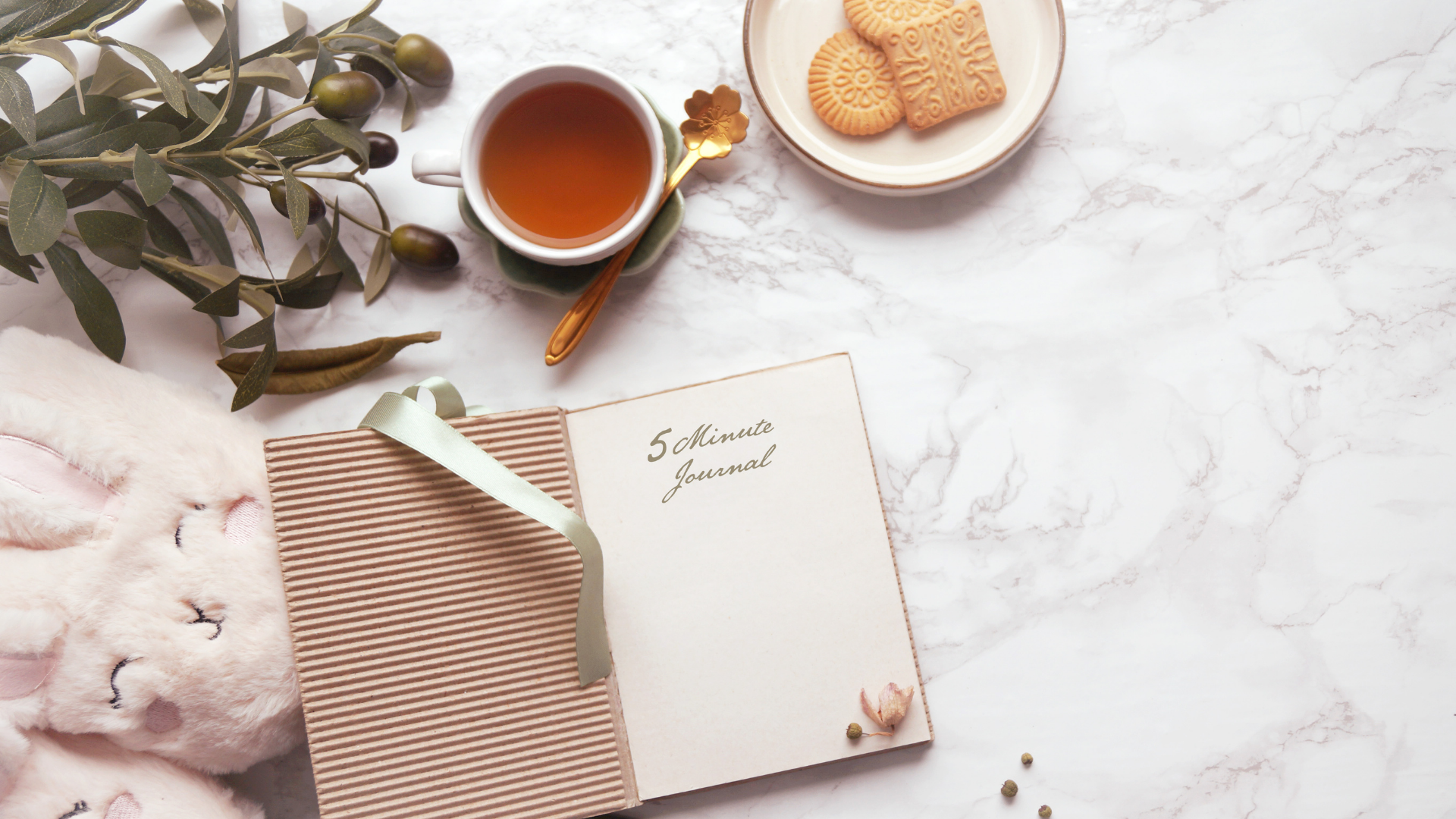 Flat-lay of tea, cookies, eucalyptus, and a striped notebook on a soft pink marble surface