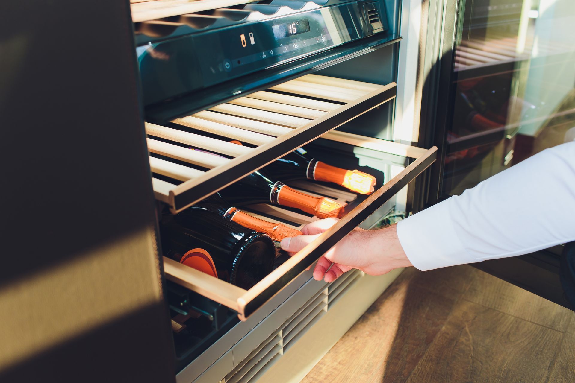 A person is taking a bottle of wine out of a wine cooler.