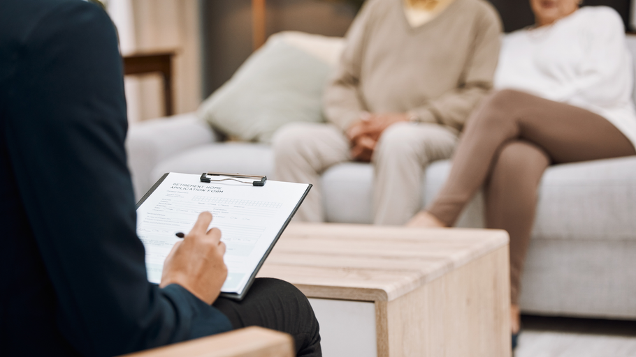 A man is sitting at a table with a clipboard in front of a couple sitting on a couch.