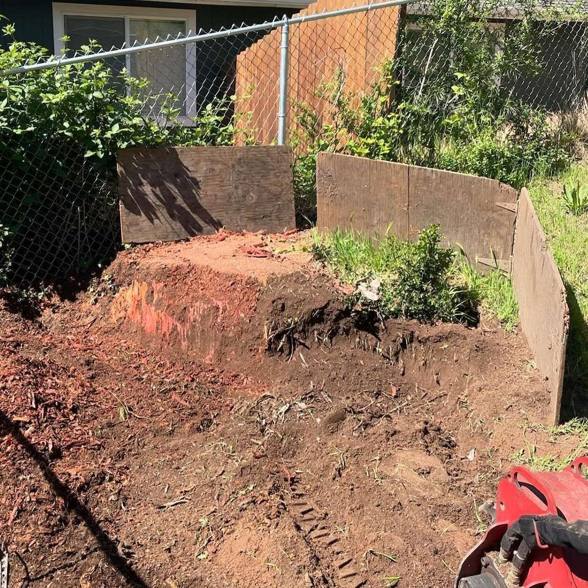 Backyard garden bed with freshly turned soil, a tree stump, and chain-link fencing behind it