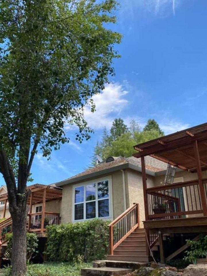 Townhouse patio with wooden stairs and railing under a large tree on a sunny day