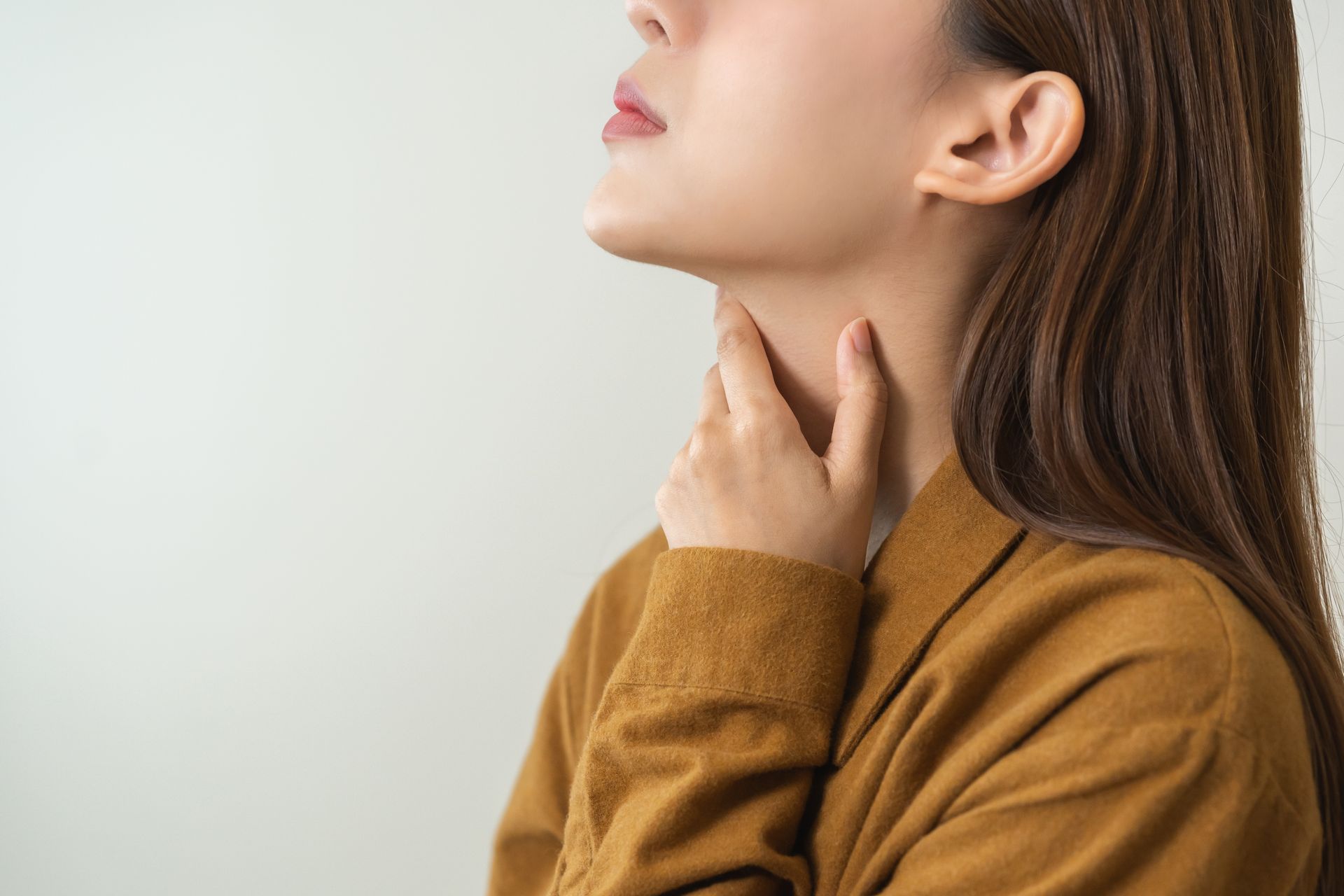 A woman is holding her throat with her hands because she has a sore throat.