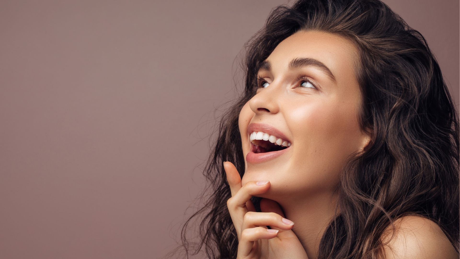 A woman with long curly hair is smiling and looking up.
