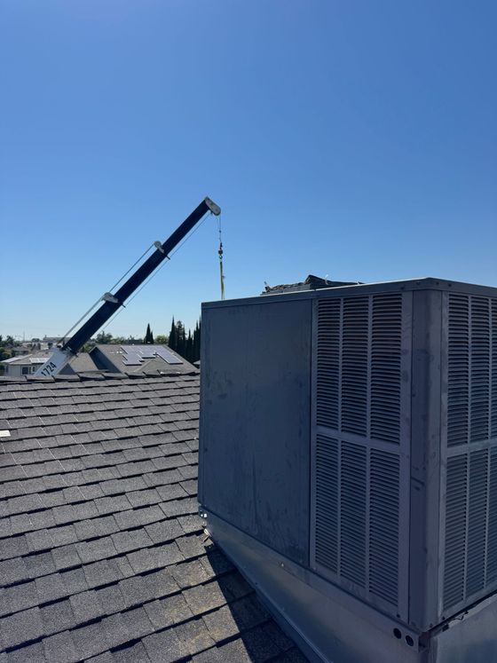 Rooftop HVAC unit beside a raised crane arm under a clear blue sky