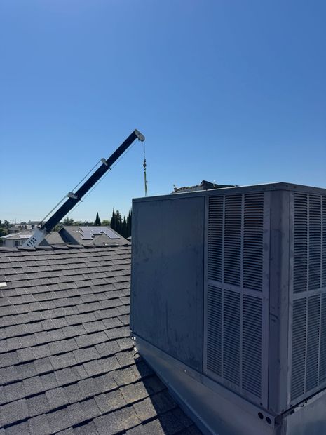 Rooftop HVAC unit beside a raised crane arm under a clear blue sky