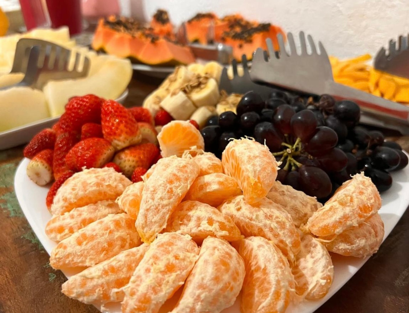 Prato de frutas variadas com laranjas descascadas, morangos, uvas e queijo sobre uma mesa