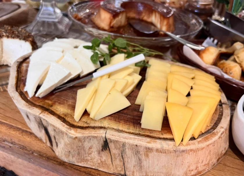 Fatias de queijo em uma tábua de madeira com fatias de pão e azeitonas sobre uma mesa.