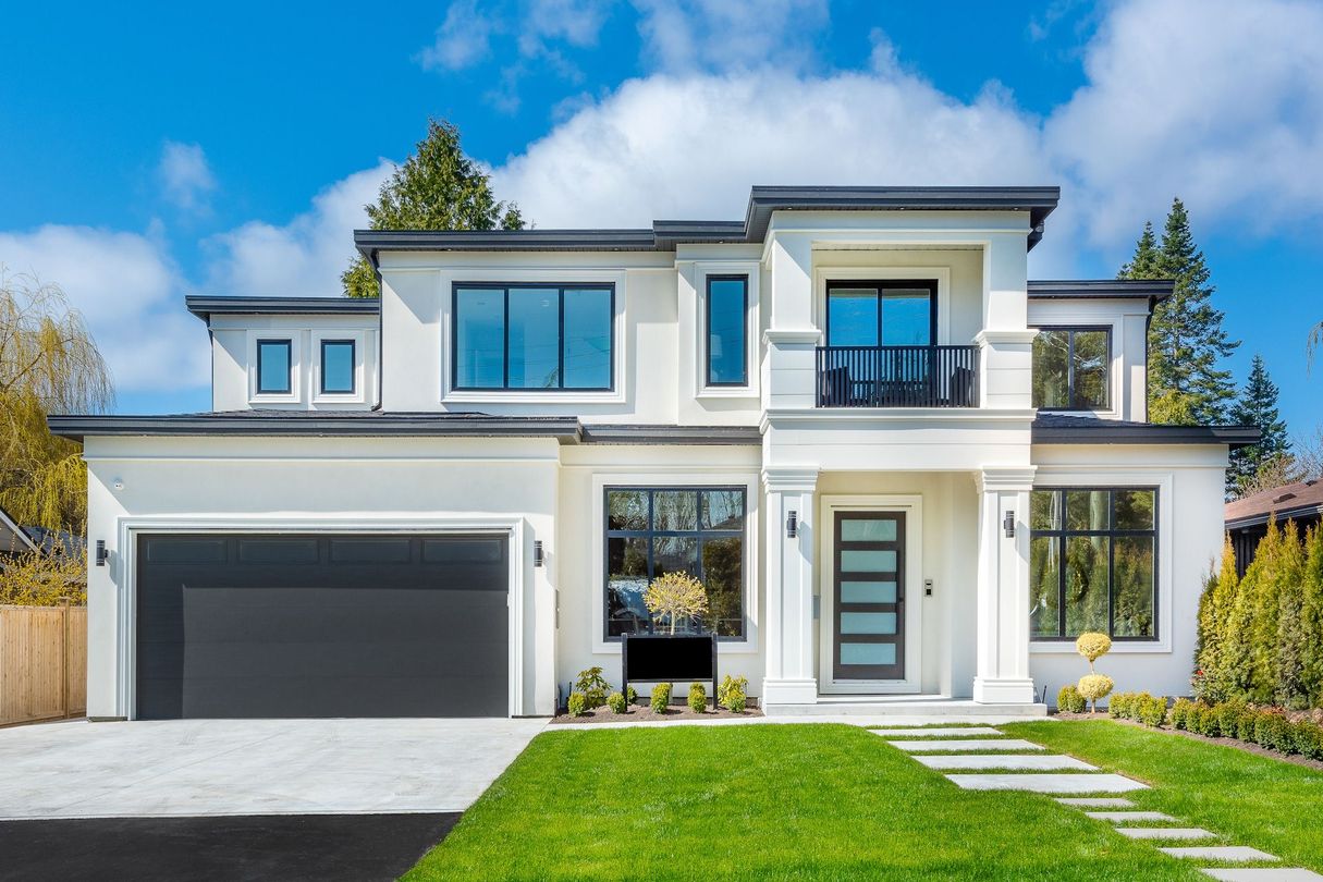 A large white house with a black garage door and a lush green lawn.
