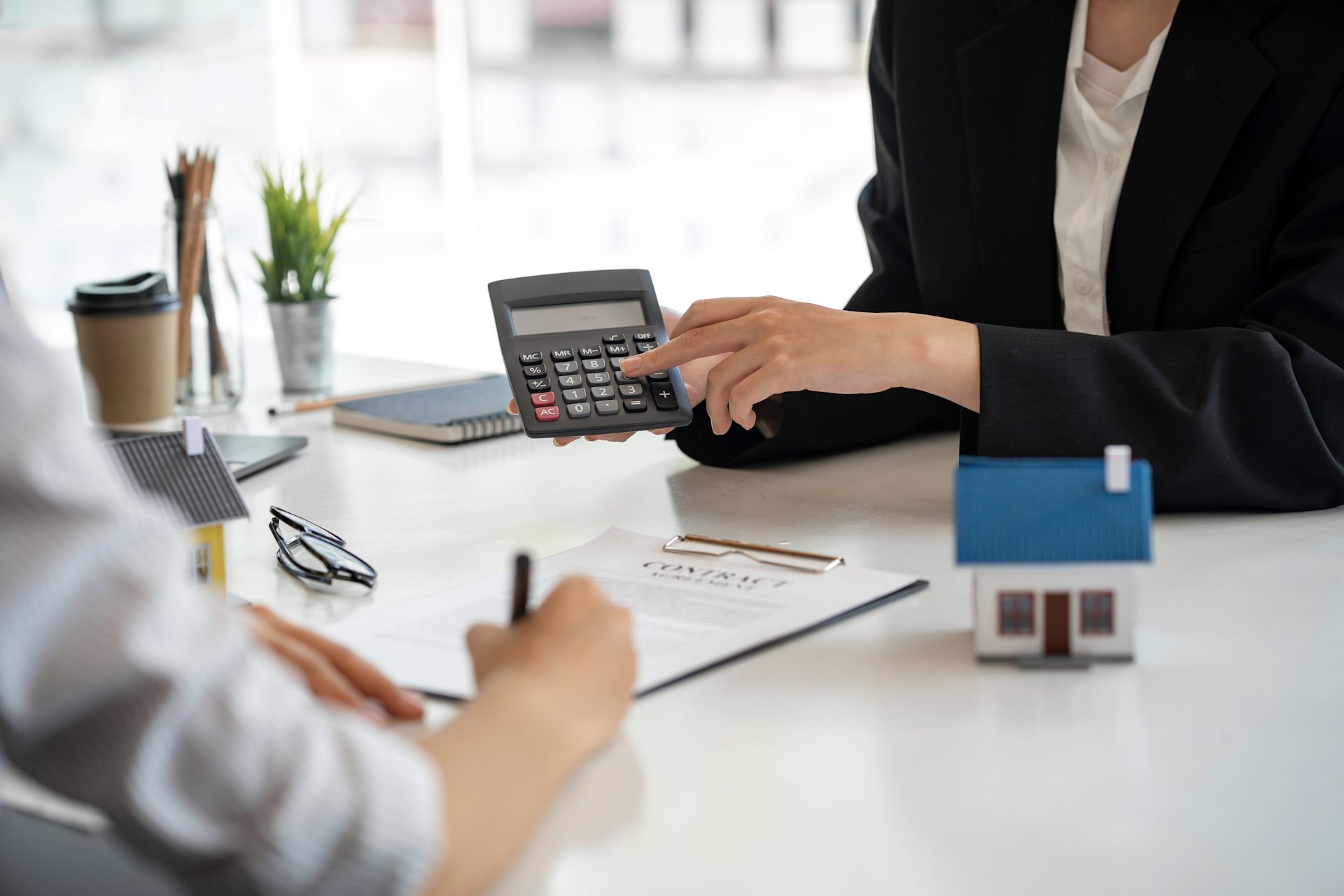 A woman is using a calculator while sitting at a table with a model house.
