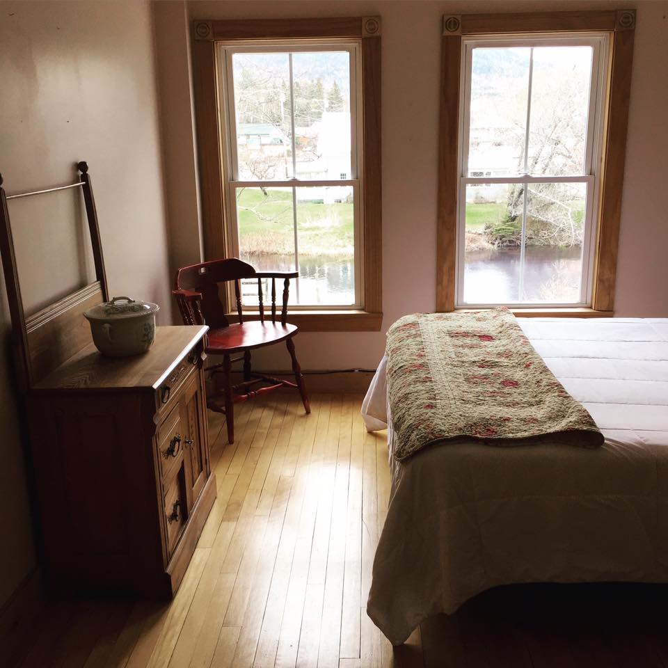 Cozy bedroom with two windows, wooden dresser and chair, and a bed with a patterned quilt