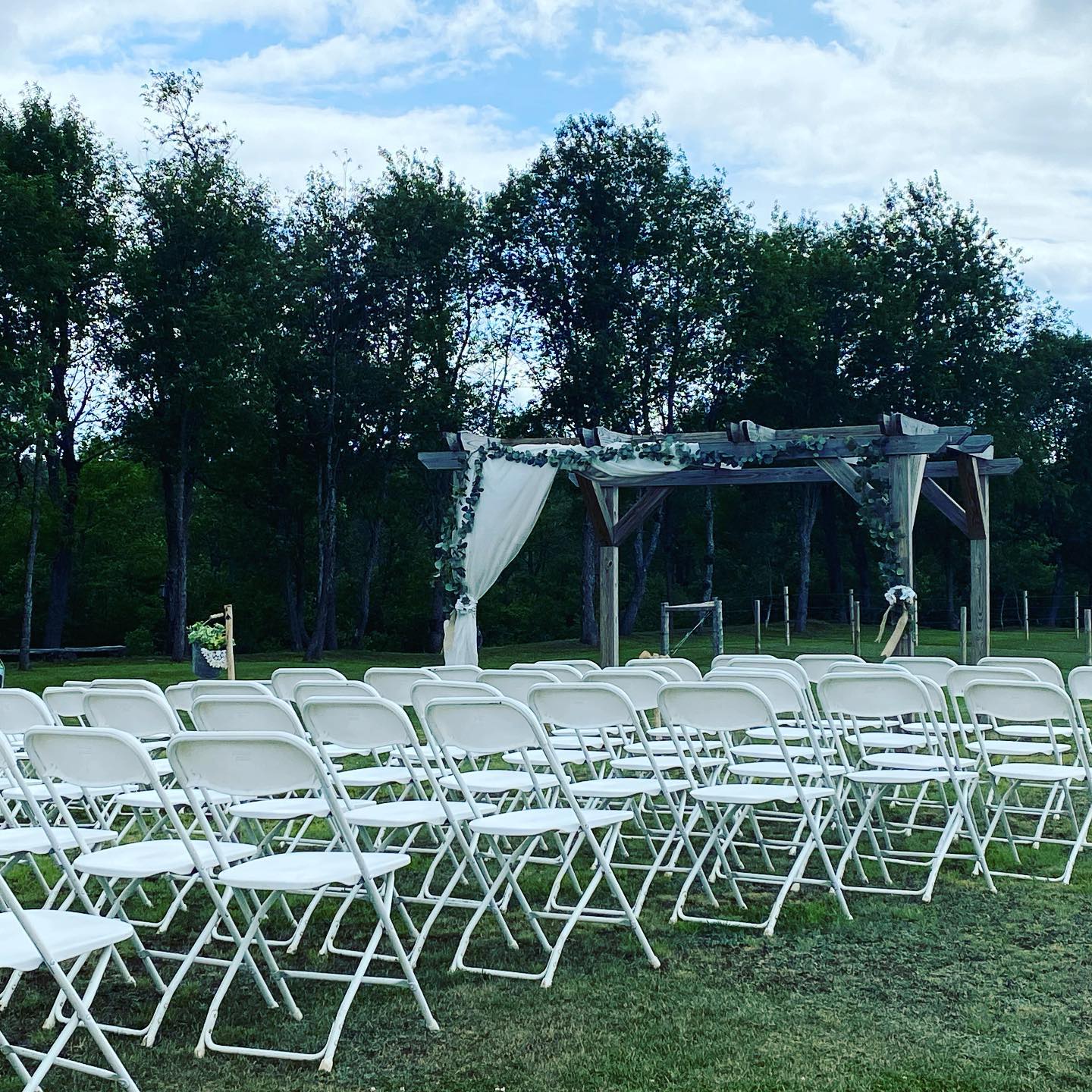 White folding chairs set up on grass for an outdoor ceremony under a small decorated arch.