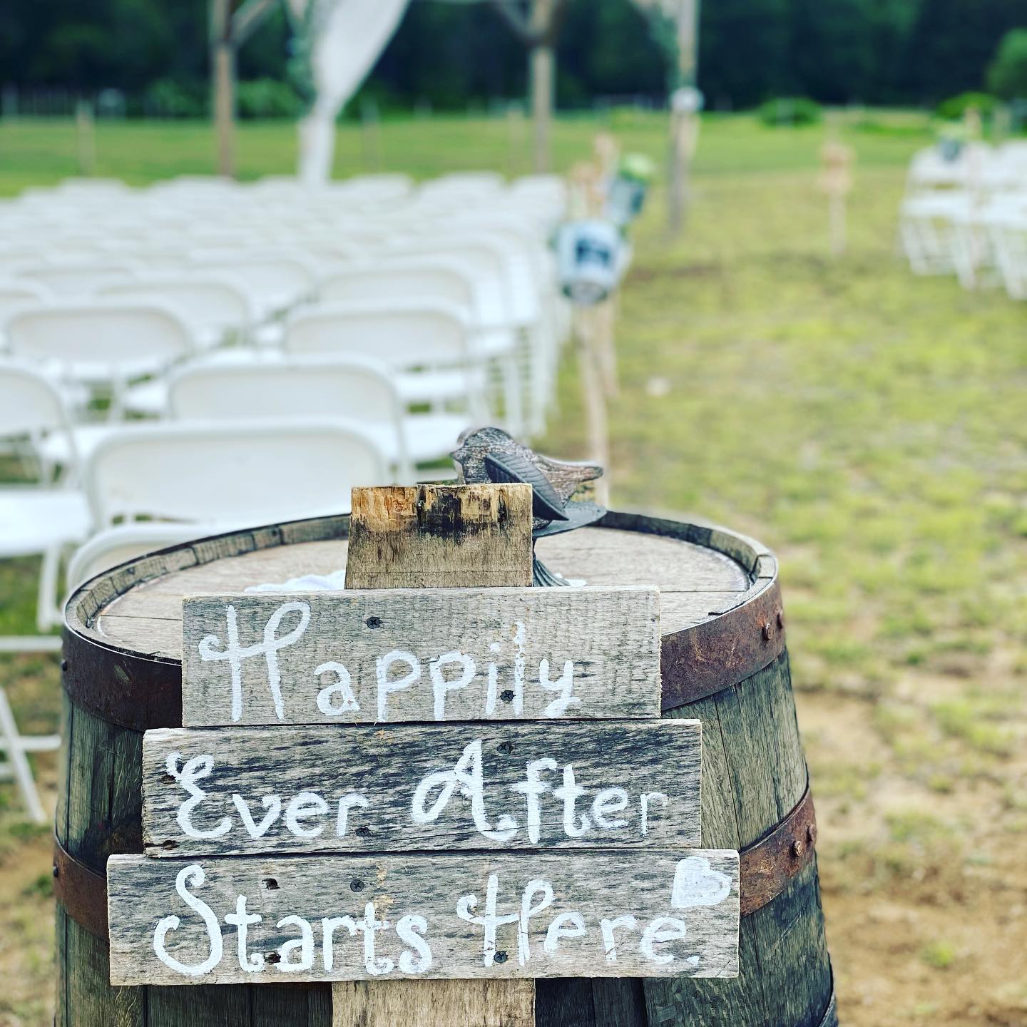 Rustic “Happy Ever After Starts Here” sign on a barrel at an outdoor wedding ceremony setup