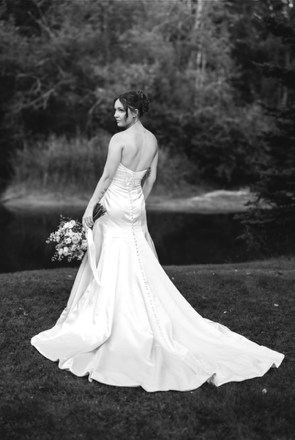Woman in a strapless white gown standing outdoors by a lake with trees in the background