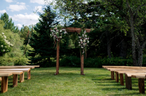 Wooden benches facing a grassy aisle under a pergola in a lush outdoor garden setting