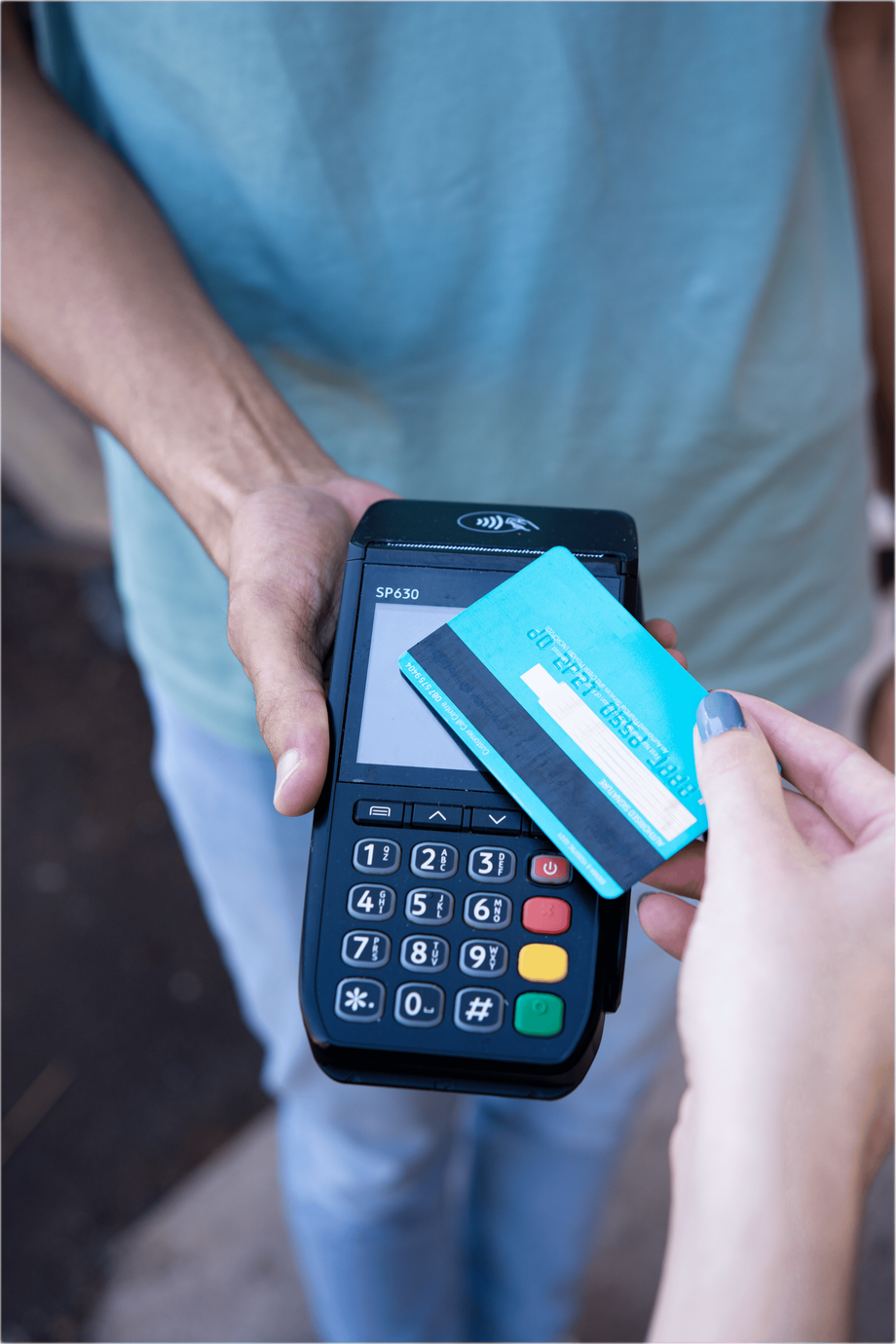A person holds a card reader while another person taps a blue payment card against the device screen.
