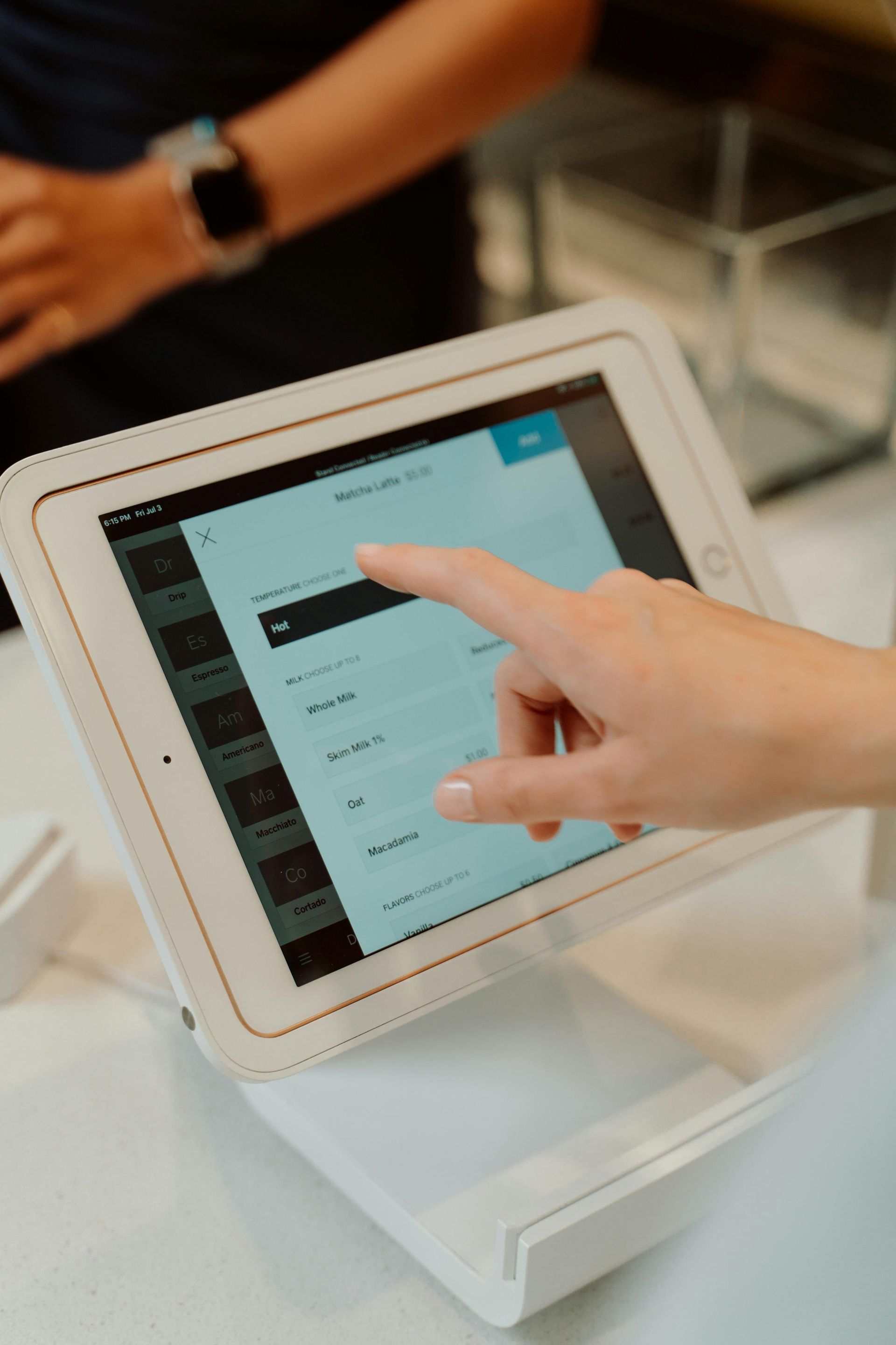 A close-up of a hand tapping a touch-screen point-of-sale terminal at a counter.