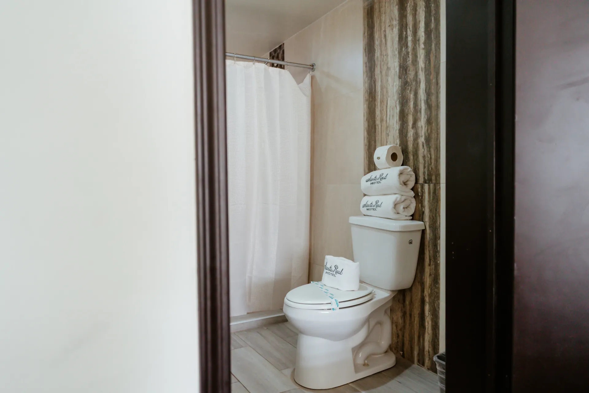 Un baño con inodoro, cortina de ducha y pilas de toallas.