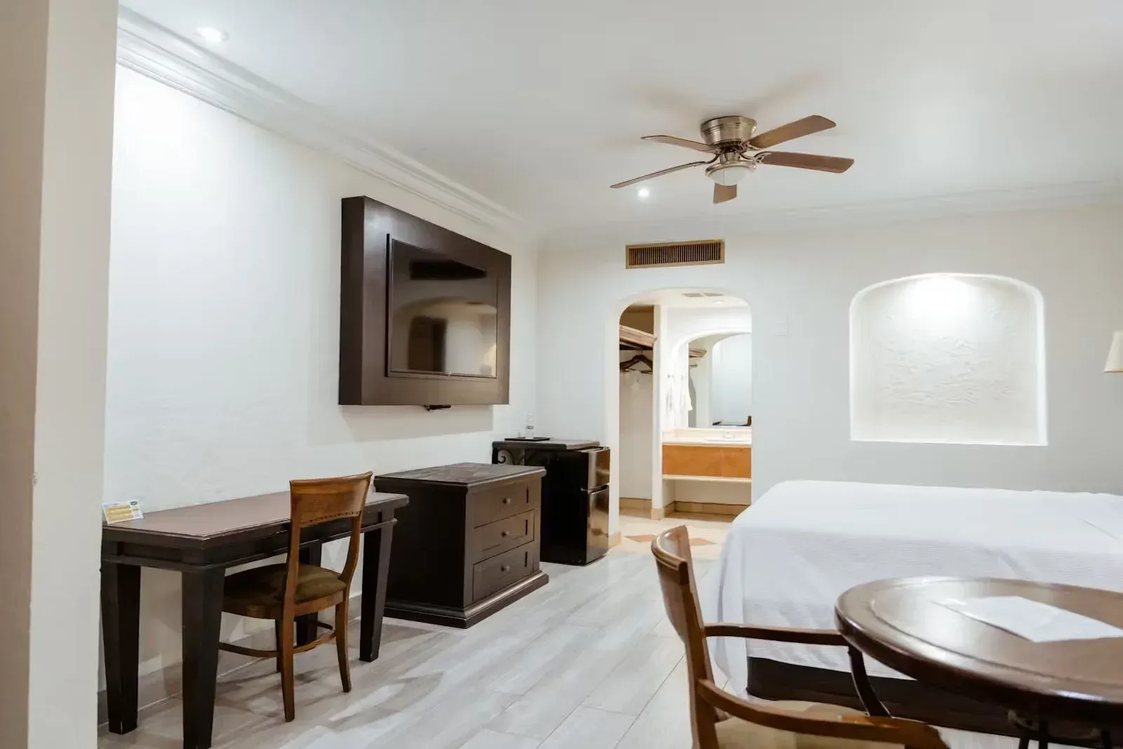 Una habitación de hotel con cama, escritorio, sillas, televisión y ventilador de techo.