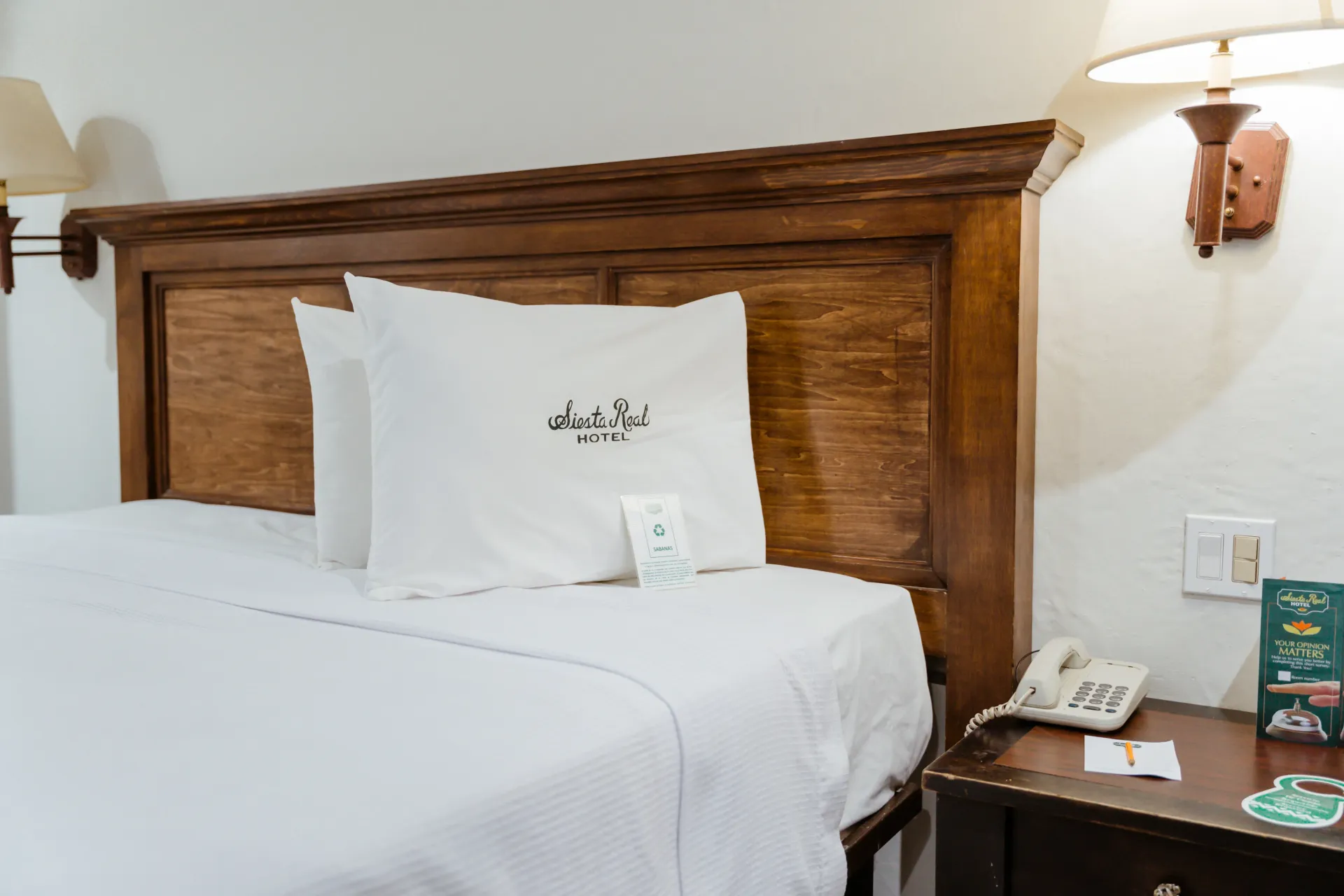 Una habitación del hotel Siesta Real Mexicana con una cama, mesita de noche, lámpara y teléfono.