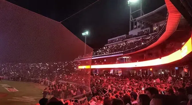 Una multitud de personas está viendo un partido de béisbol en un estadio por la noche.