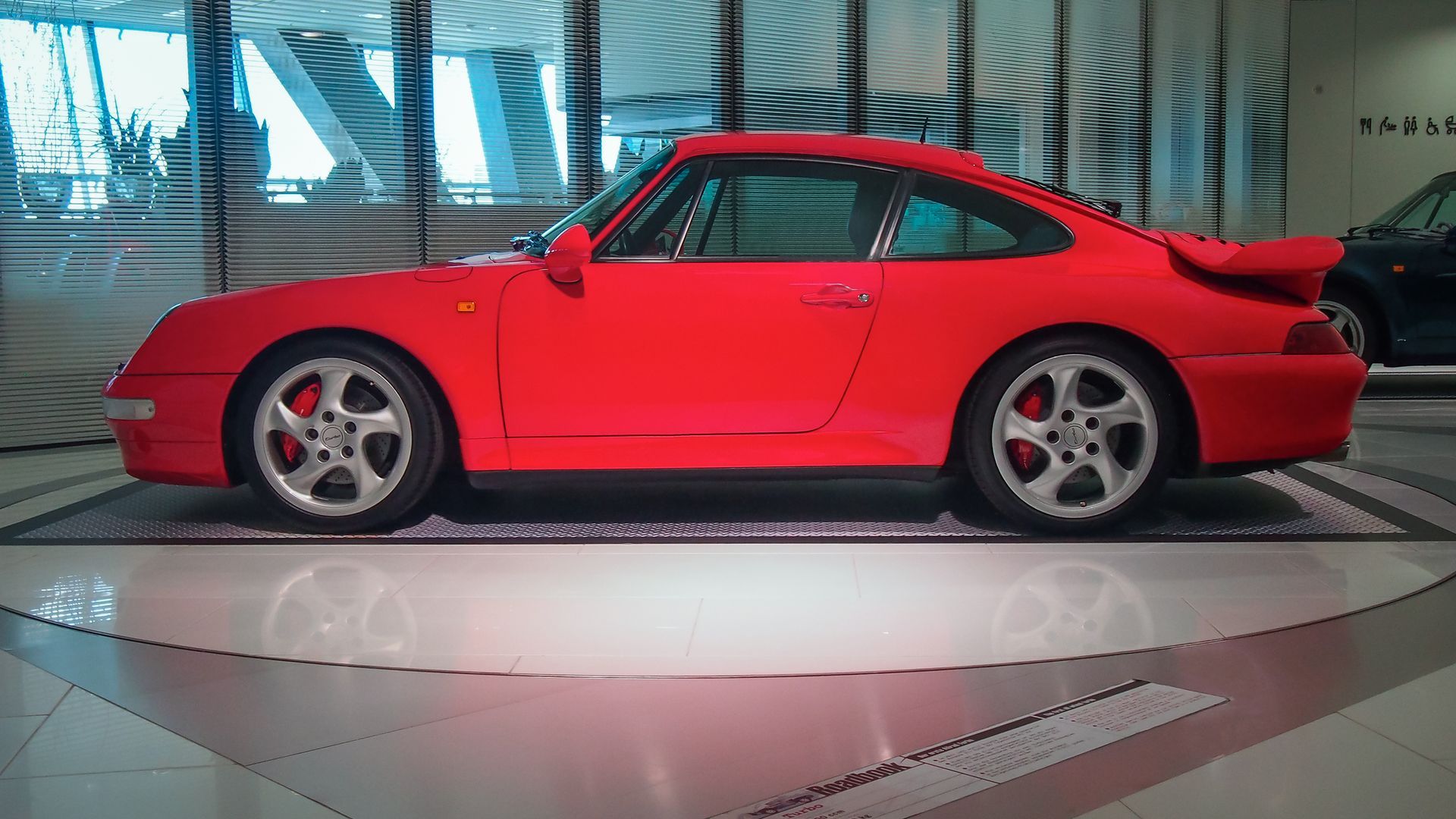 Ein schwarzer Porsche 993 parkt bei einem sonnigen Autotreffen im Freien, umgeben von anderen Sportwagen.