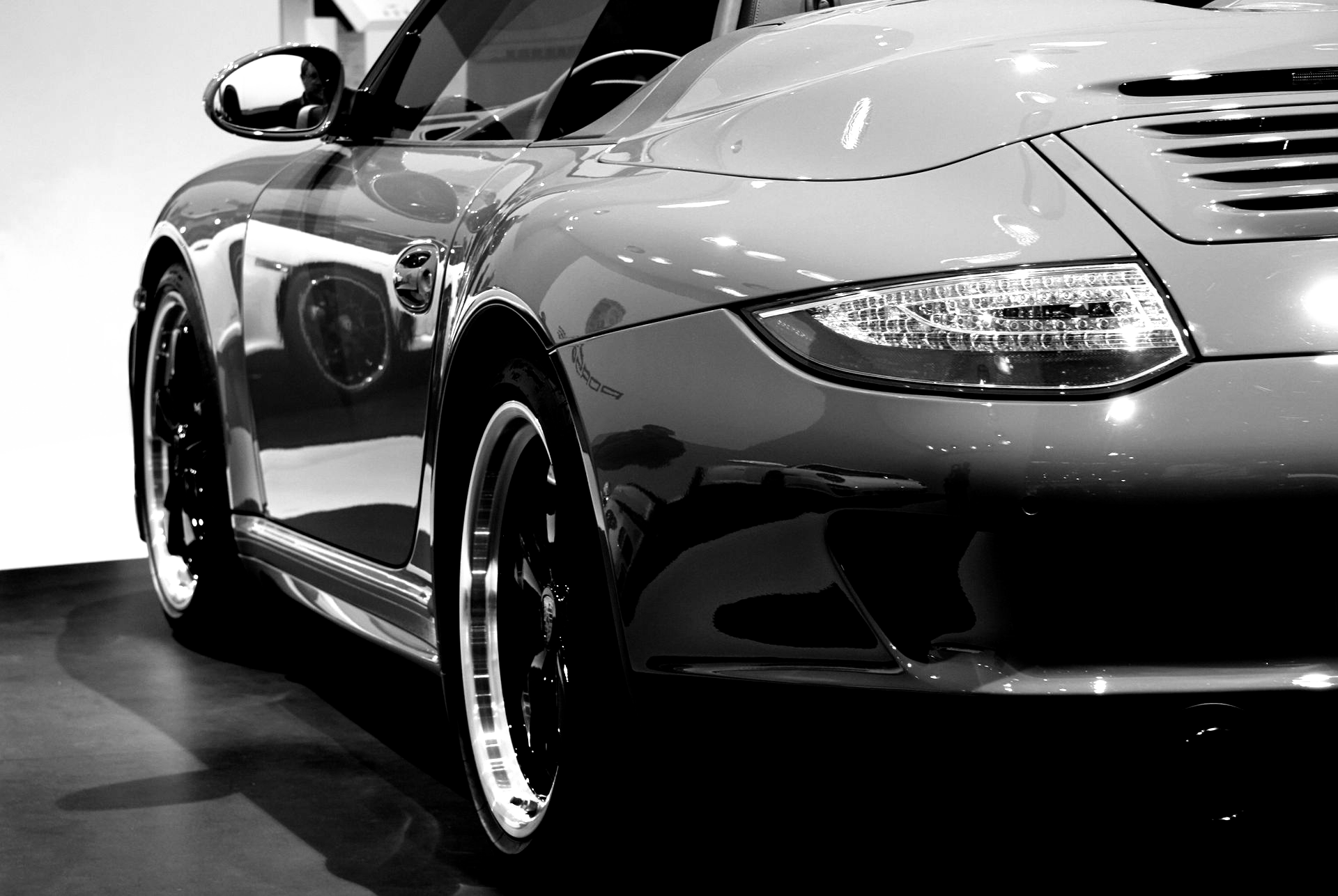 Ein grauer Porsche Targa fährt auf einer Stadtstraße, gefolgt von einem grauen Auto und einem Motorrad im Verkehr.