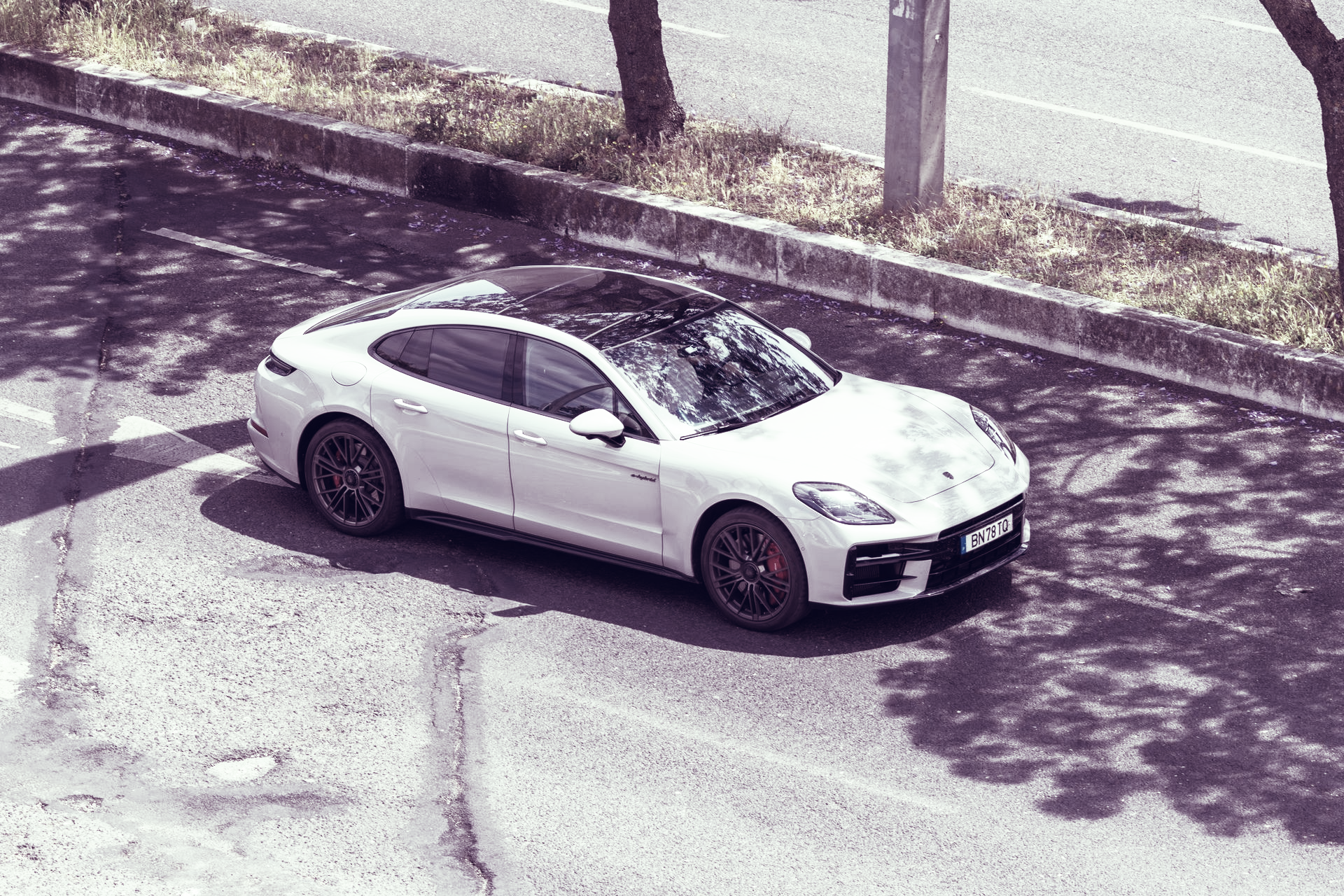 Ein schwarzer Porsche Panamera, der bei Sonnenuntergang an einer Küstenstraße parkt und leuchtenden Rücklichtstreifen