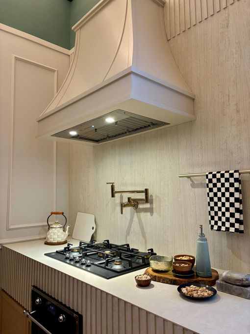 Kitchen with range hood, stovetop, and accessories. White and wood tones create a warm interior.