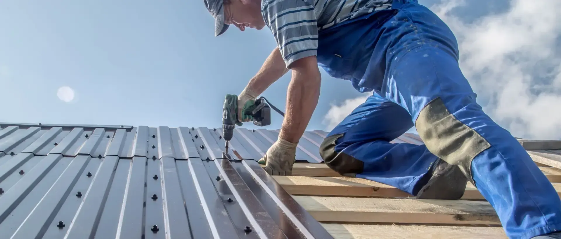 Workers on a large corrugated metal roof under a cloudy sky