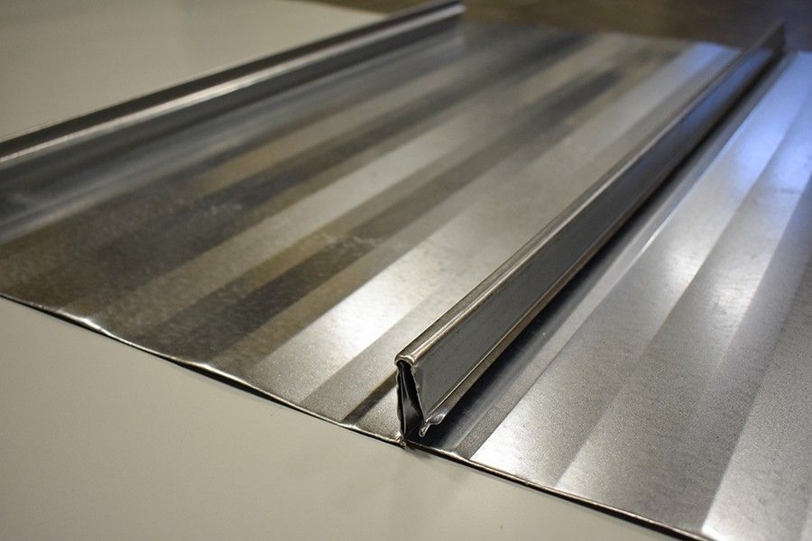 Two screws on a gray metal surface, one shiny silver and one rusty brown.