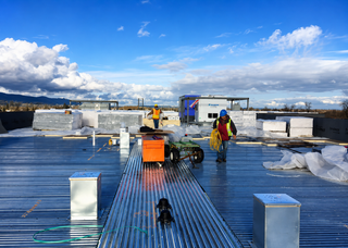 Worker installing black roofing felt on a flat roof with a torch applicator.