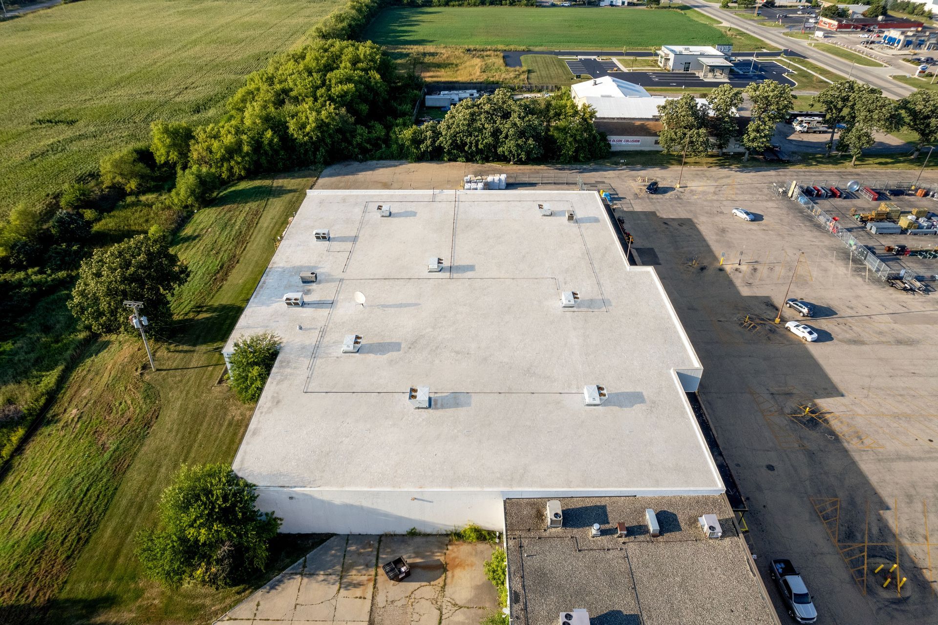 Aerial view of a white-roofed building with parked cars and trees around it.