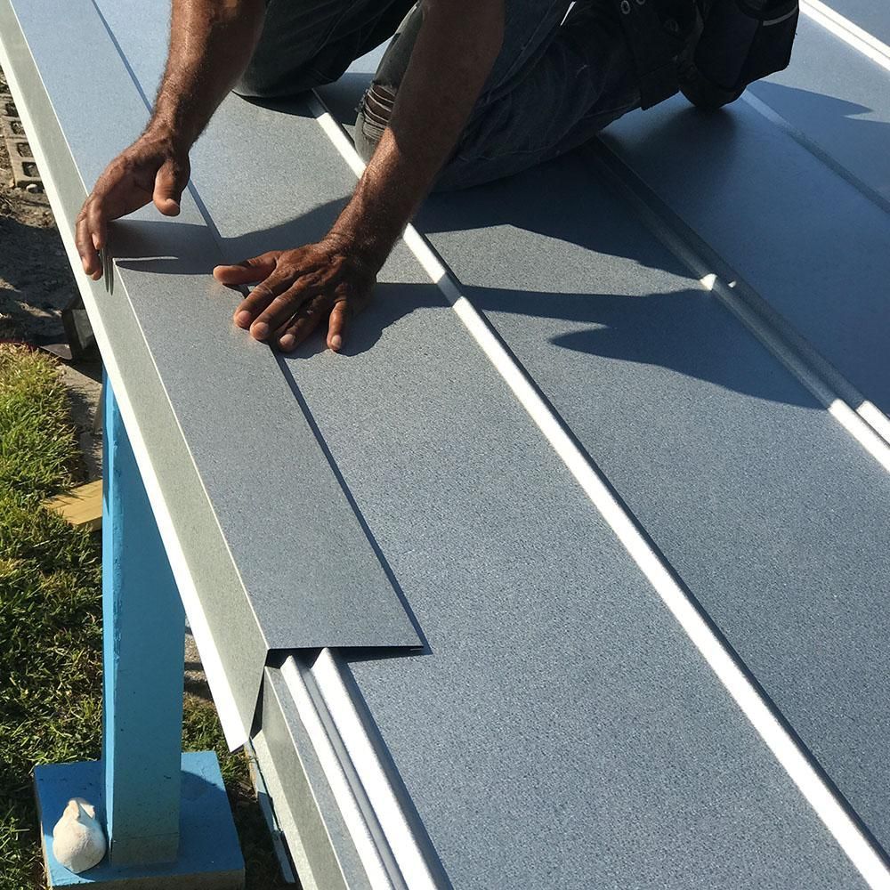Worker in green shirt kneeling on a rooftop, smoothing a white surface with gloved hands.