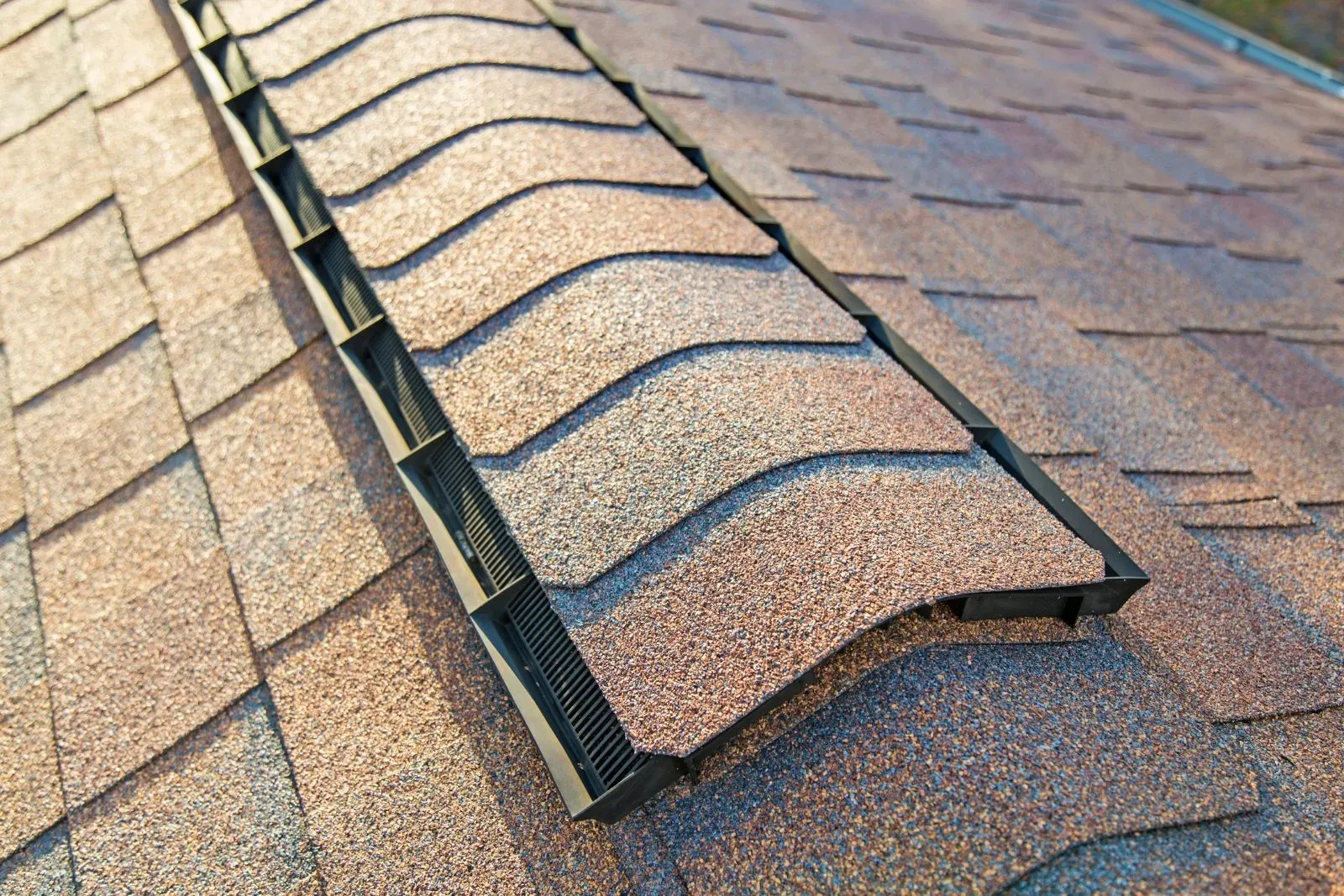 Close-up of a brown shingled roof with a central ridge vent under daylight