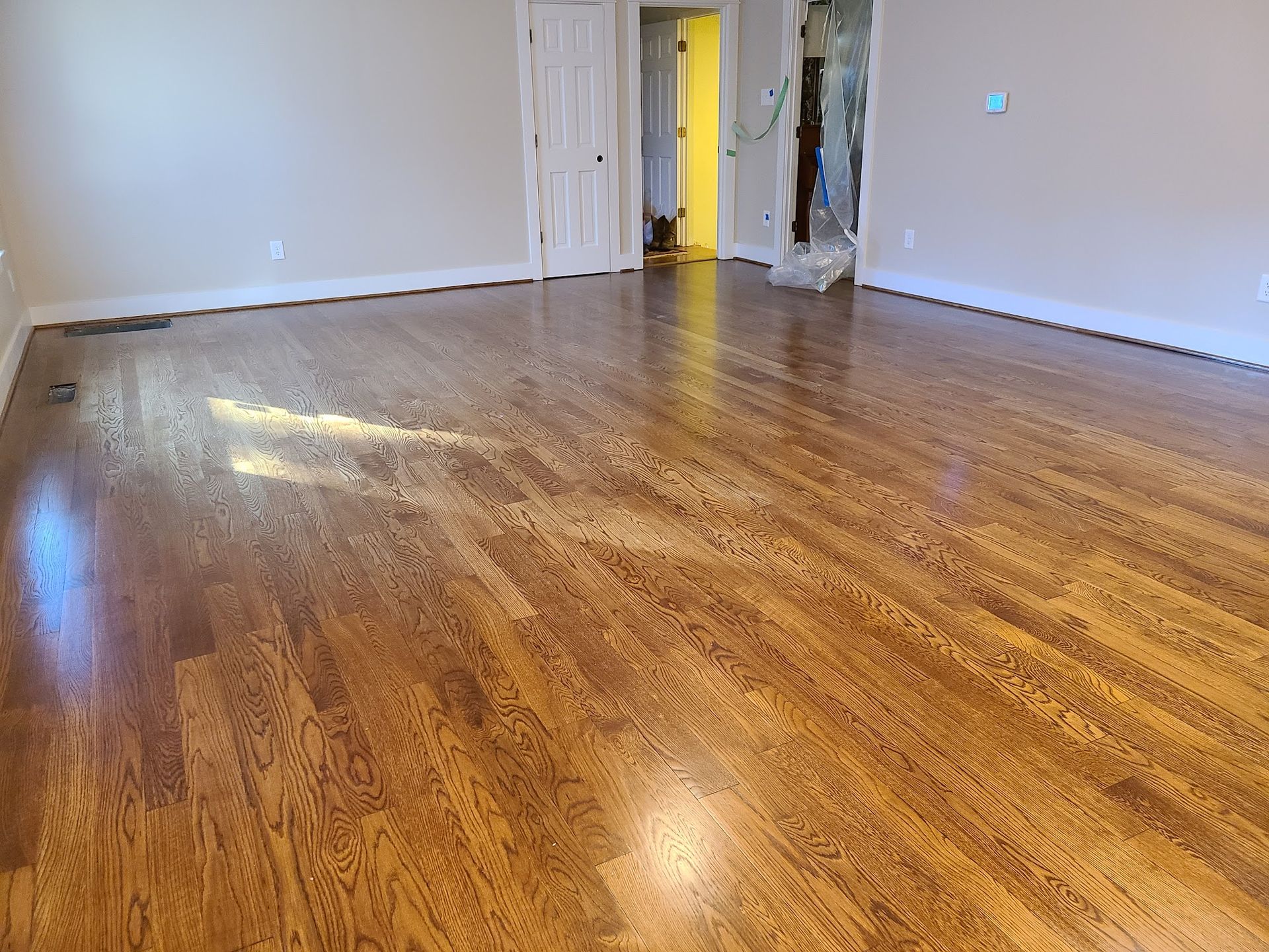 Newly refinished hardwood floor in a room with white trim, tan walls, and a partially open doorway.