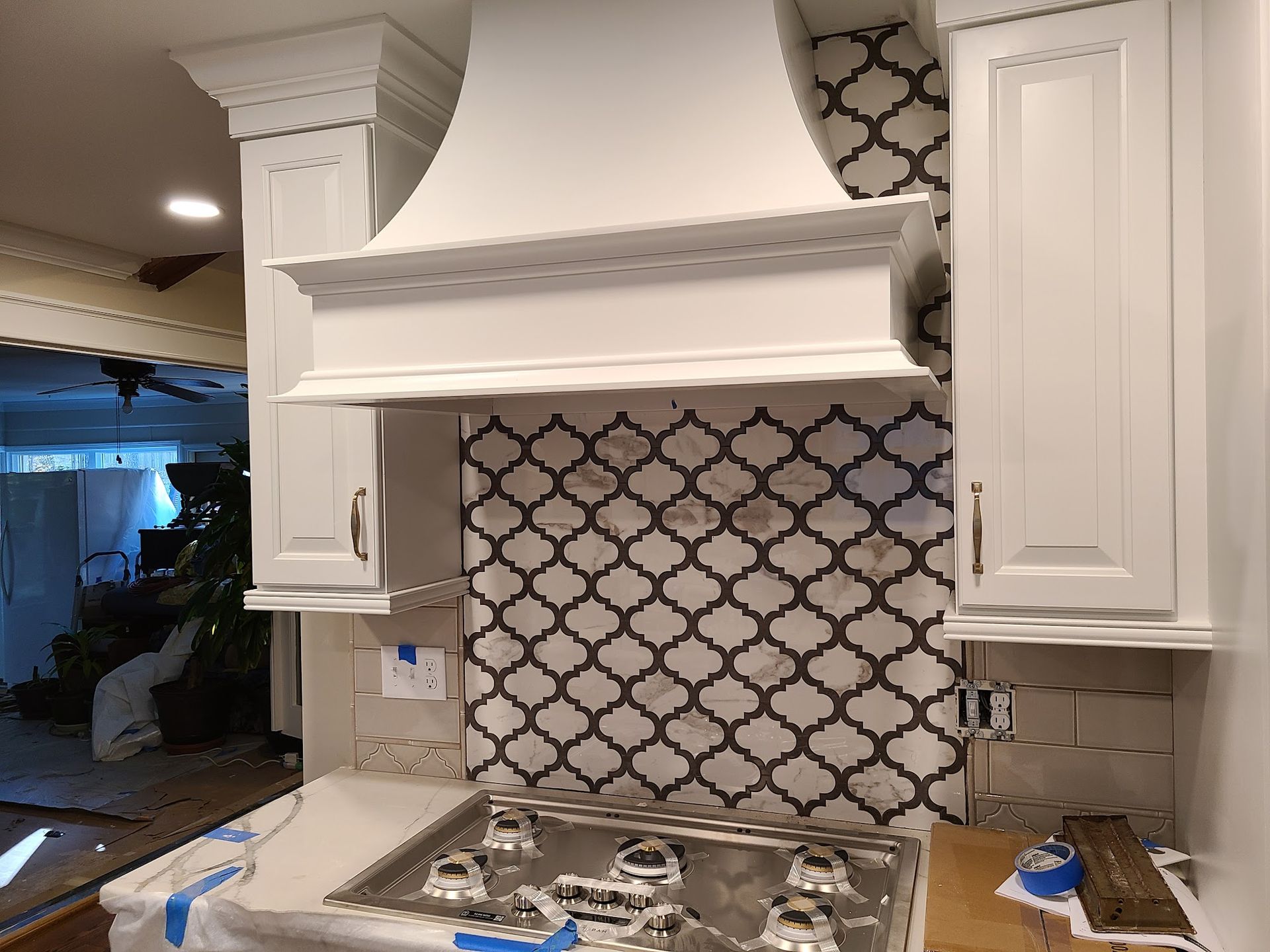 White kitchen range hood with tile backsplash and stove. Cabinets on either side.