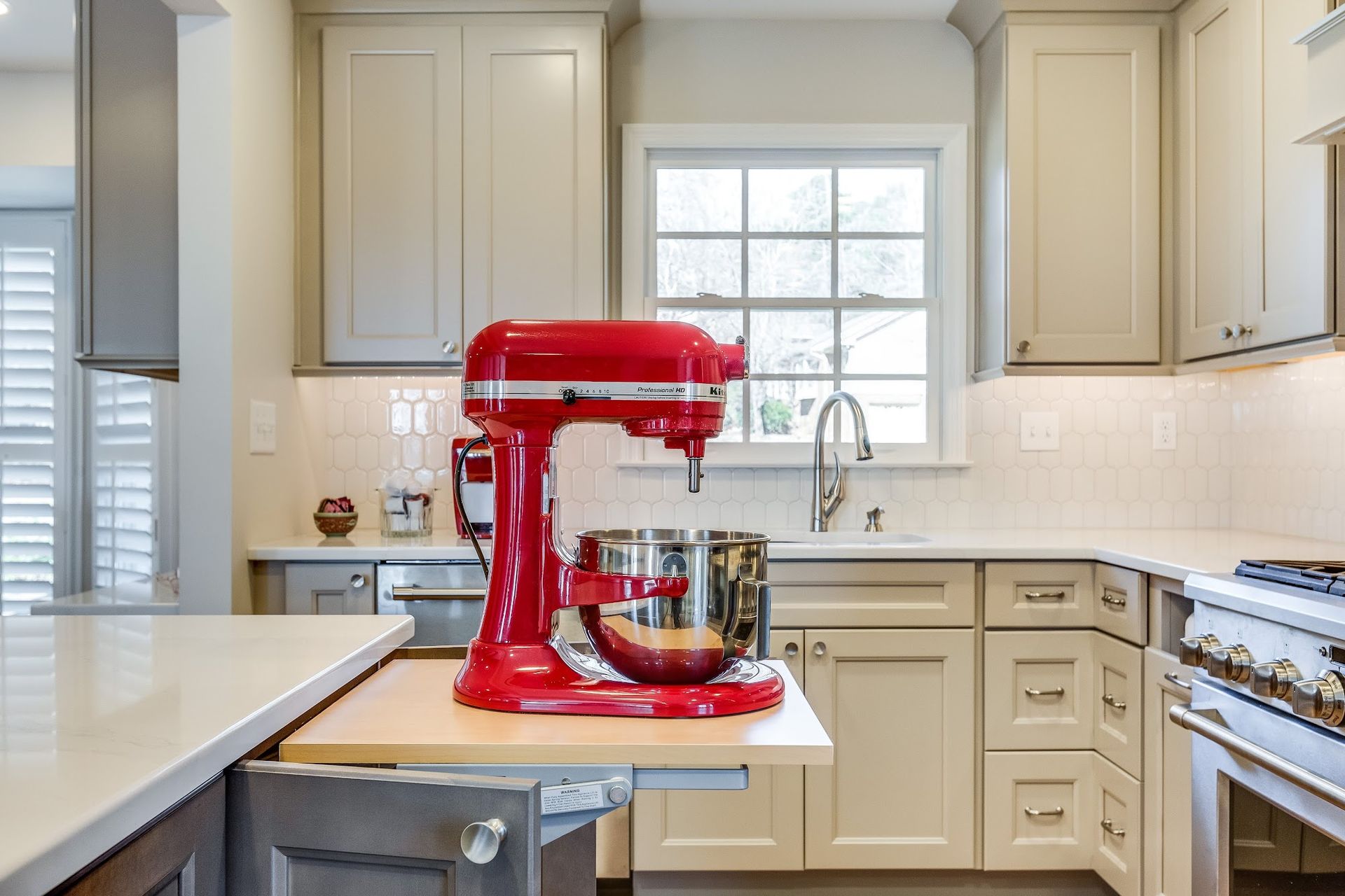 Red KitchenAid mixer on a pull-out shelf in a cream-colored kitchen.