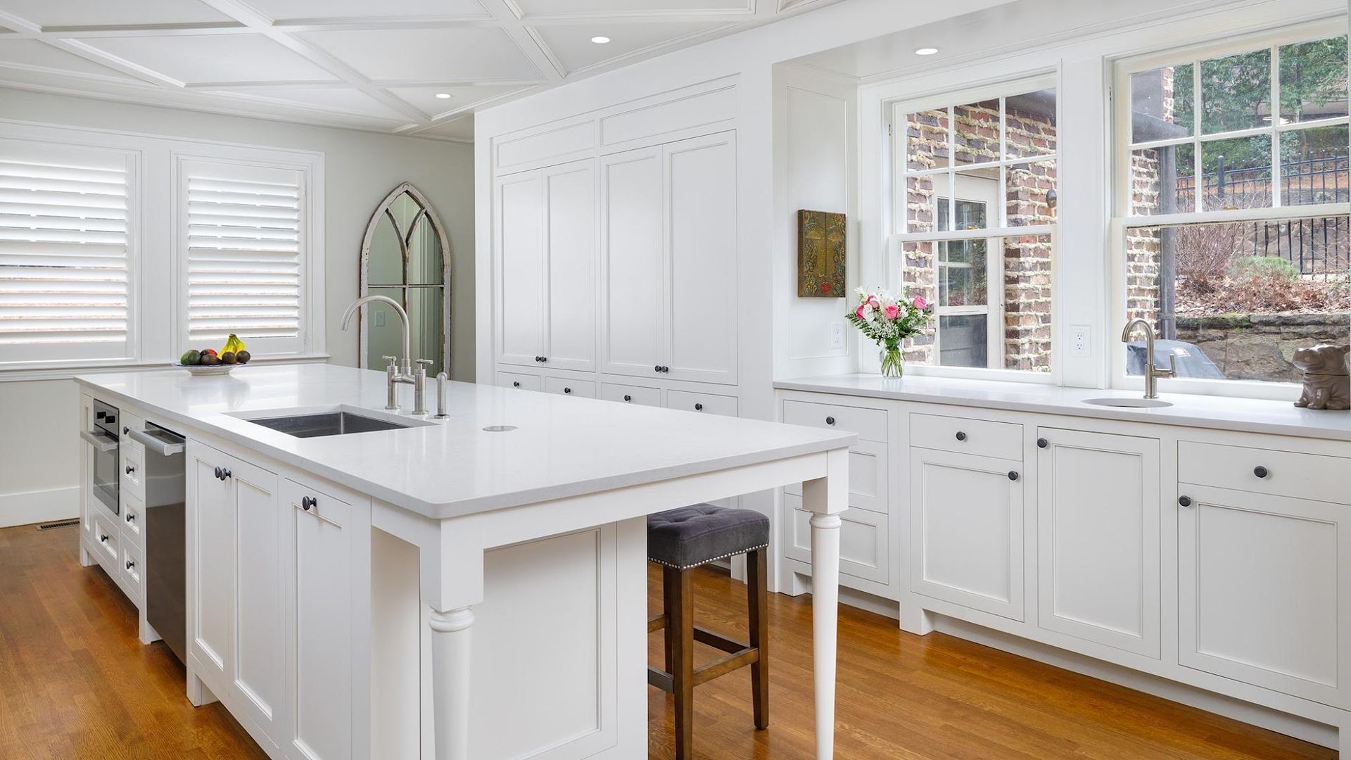 White kitchen with island, cabinets, windows, and wood floors.