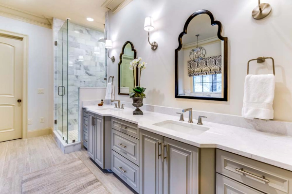Bathroom with gray cabinets, white countertop, ornate mirrors, and a glass shower.
