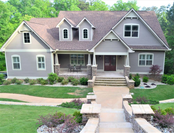 Two-story house with gray siding, brown roof, and stone accents. Front porch, walkway, and green lawn.