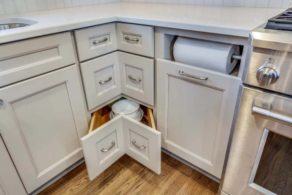 White kitchen cabinets with open drawers holding dishes and a paper towel roll.