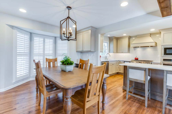 Dining room with wooden table and chairs, adjacent to a kitchen with light-colored cabinets and hardwood floors.