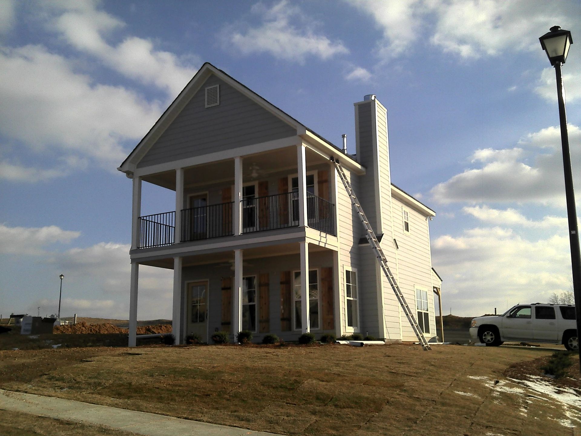 Two-story house under construction with a chimney, a ladder, and a pickup truck on a sunny day.