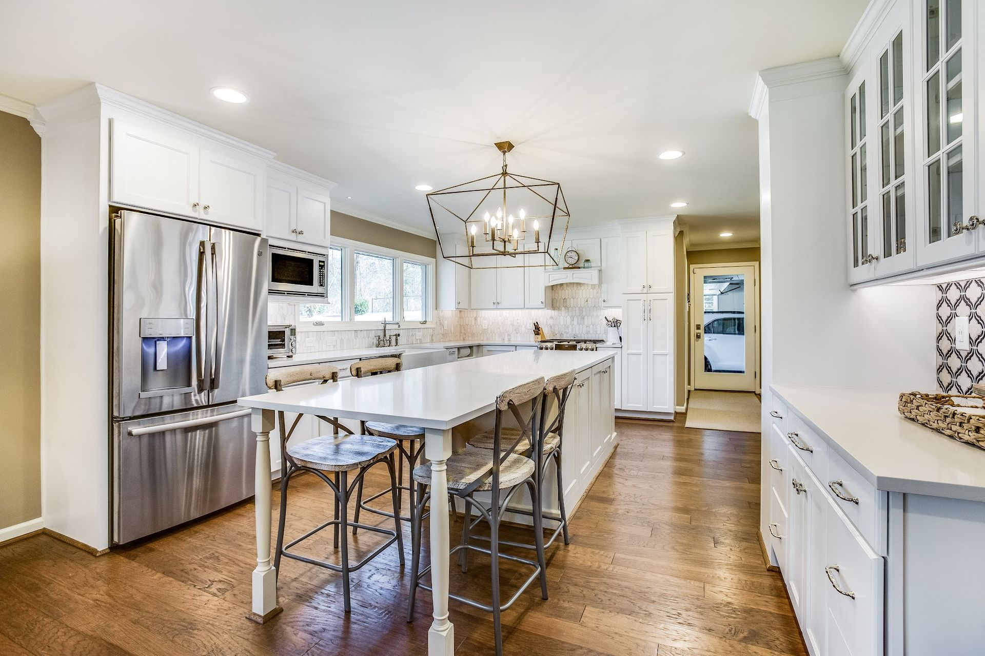 Bright white kitchen with stainless steel appliances, white island with stools, and hardwood floors.