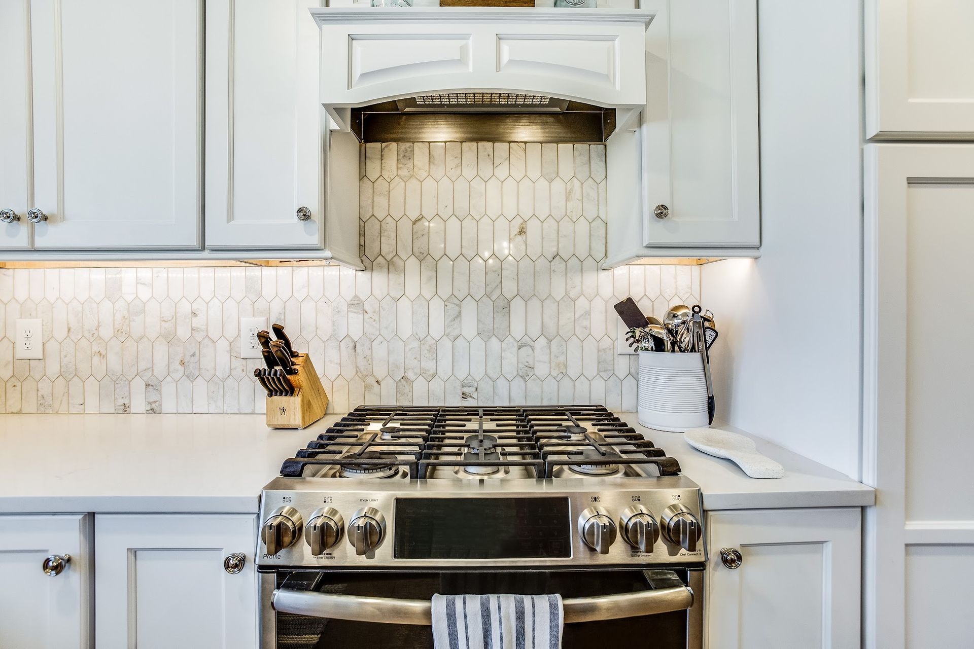 Kitchen with white cabinets, stainless steel range, and tile backsplash.