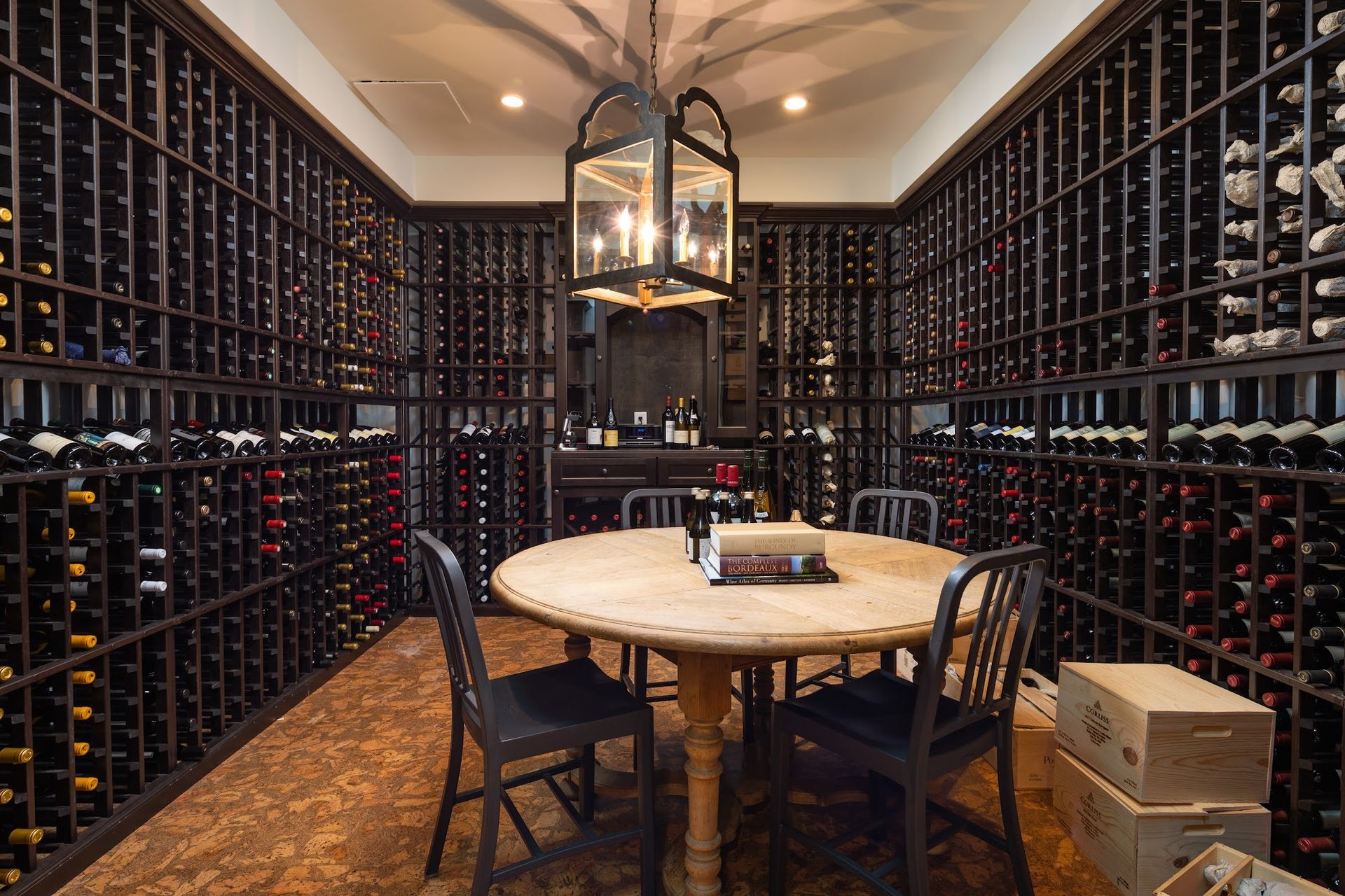 Wine cellar with wooden racks, round table, chairs, and hanging lantern.