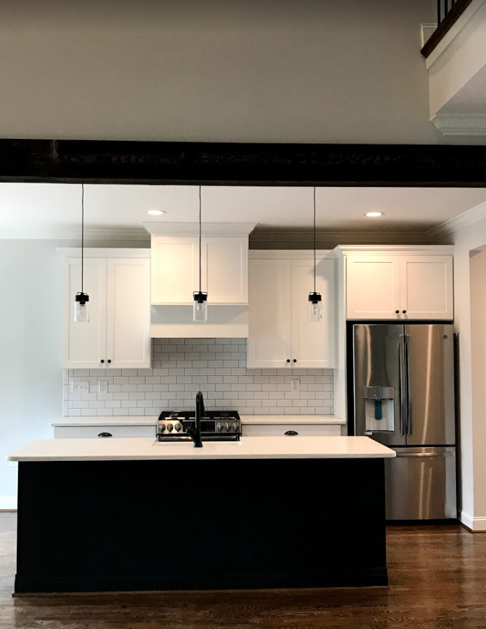 Modern kitchen with a black island, white cabinets, and stainless steel refrigerator.